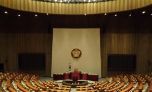 대한민국 국회 본회의장 내부 전경. 붉은 카페트가 깔린 중앙 발언대와 의장석, 그 앞을 반원형으로 둘러싼 국회의원 좌석들이 웅장하게 펼쳐져 있어 합의와 견제, 절차적 정당성에 기반한 민주주의 의회 권력을 상징하는 실내 사진